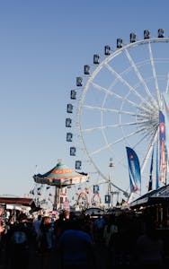 A bustling day at Stuttgart fairground featuring a towering Ferris wheel and carnival rides.
