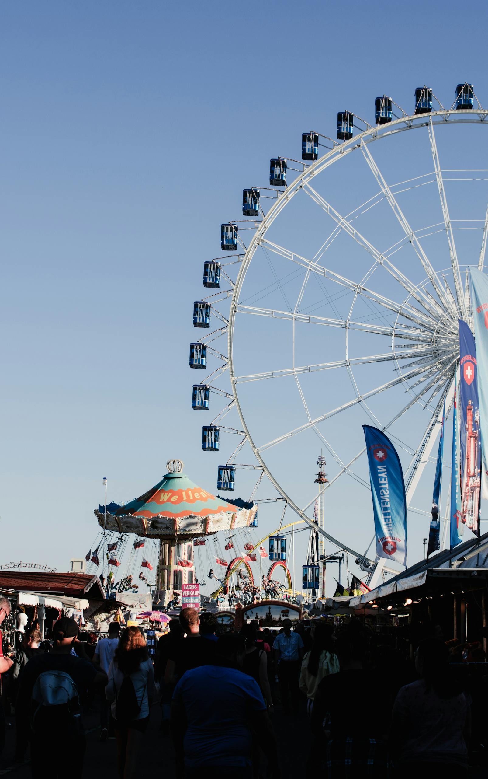 A bustling day at Stuttgart fairground featuring a towering Ferris wheel and carnival rides.
